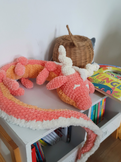 Peluche dragon corail en laine posée en boule sur une table – création artisanale Les Doudous de Woolfy