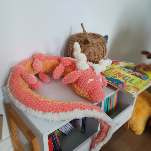 Peluche dragon corail en laine posée en boule sur une table – création artisanale Les Doudous de Woolfy