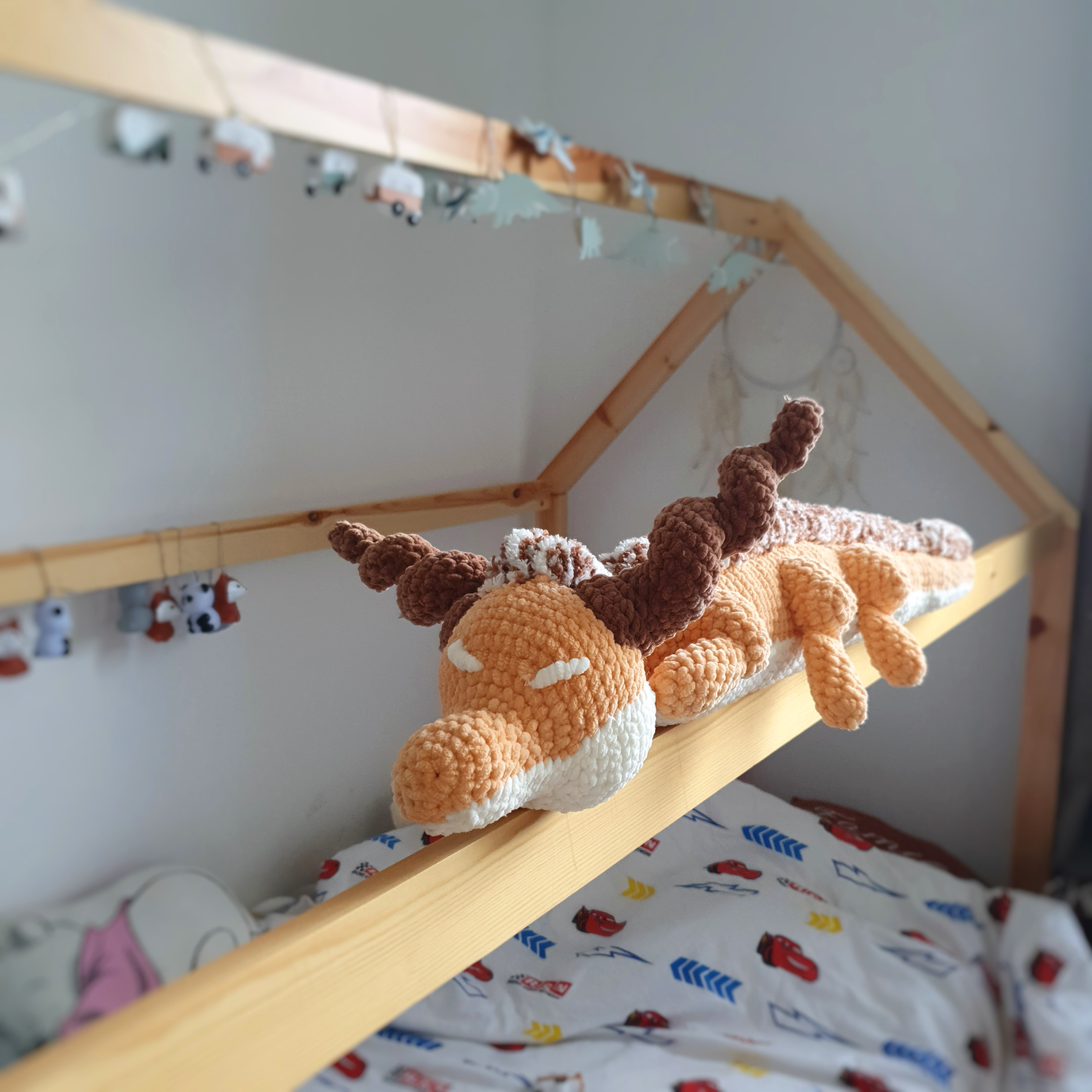 Gros plan sur la tête du grand dragon orphelin orange en laine, posé sur une barre de lit – Les Doudous de Woolfy