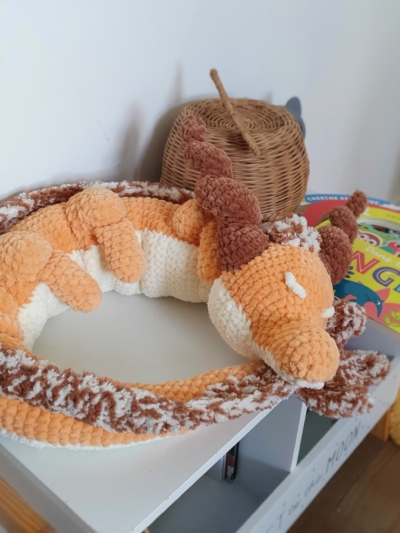 Grand dragon orphelin orange en laine fait main, posé en boule sur une table – création Les Doudous de Woolfy