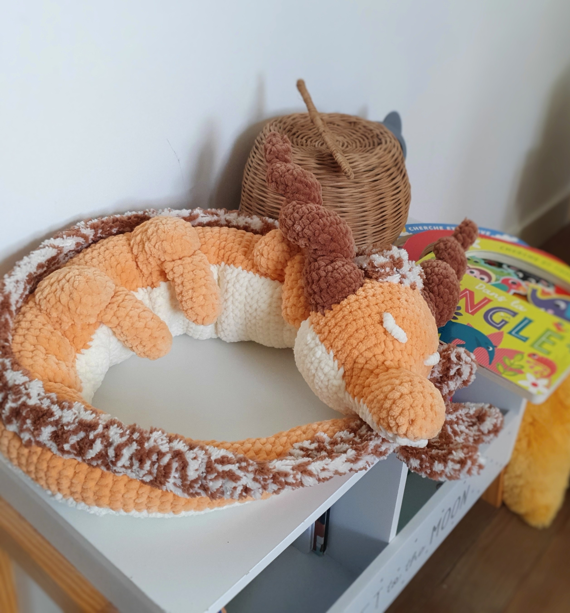 Grand dragon orphelin orange en laine fait main, posé en boule sur une table – création Les Doudous de Woolfy
