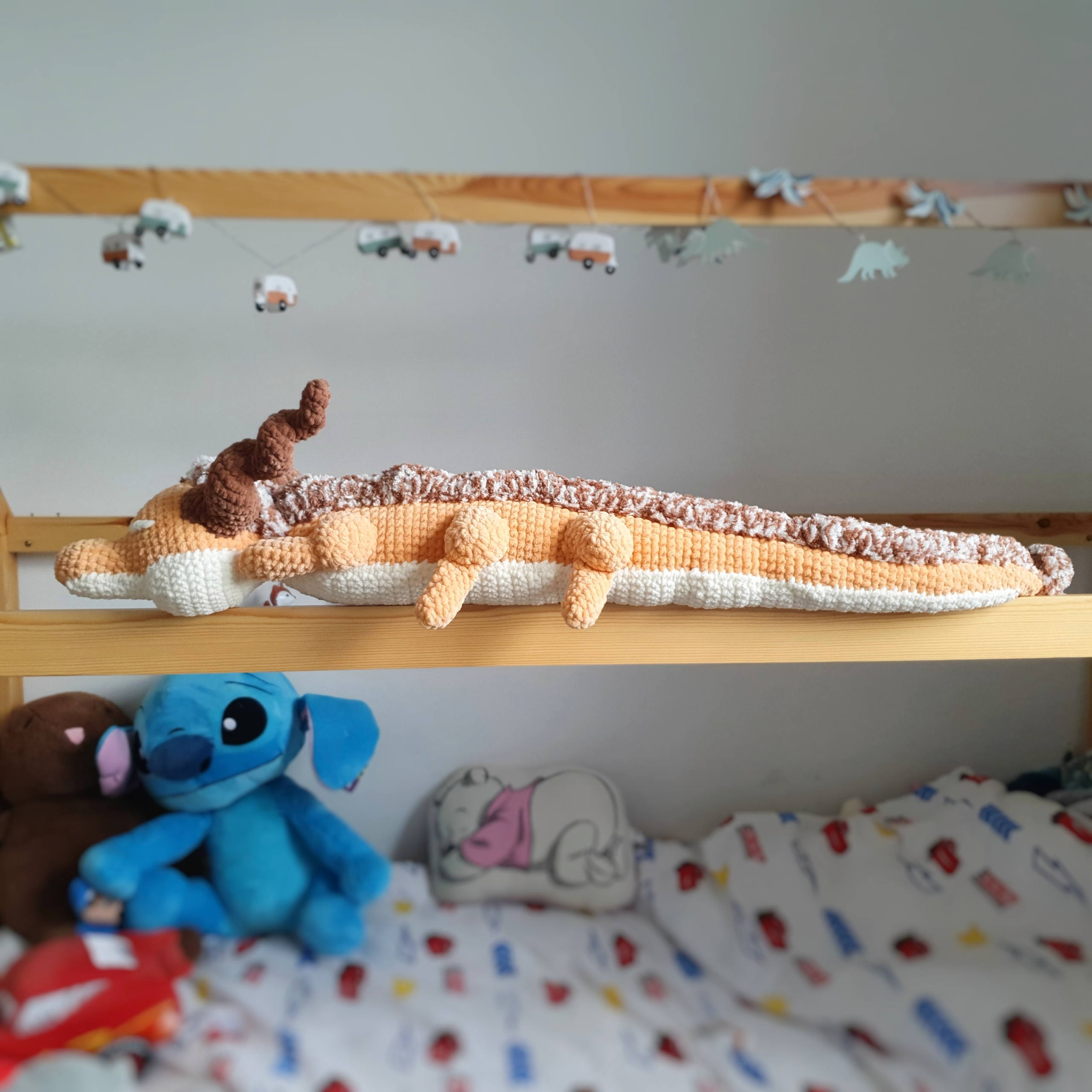Grand dragon orphelin orange en laine, posé sur une barre de lit – création artisanale Les Doudous de Woolfy