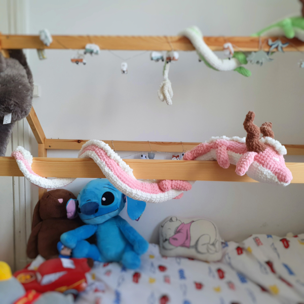 Dragon orphelin rose en laine crochetée à la main, enroulé autour d’une barre de lit – Les Doudous de Woolfy