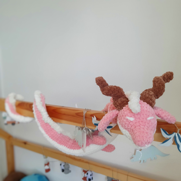 Dragon orphelin rose en laine crochetée à la main, enroulé autour d’une barre de lit – Les Doudous de Woolfy