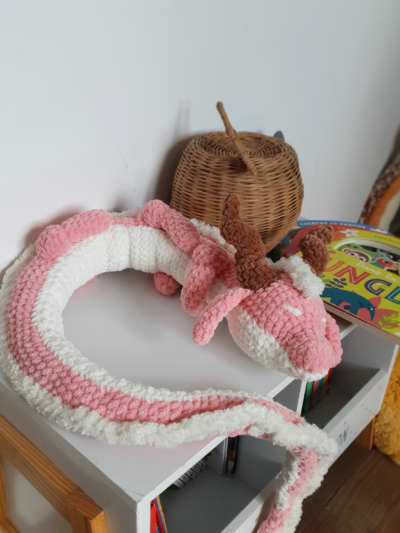 Dragon orphelin rose en laine fait main, posé en boule sur une table – création artisanale Les Doudous de Woolfy