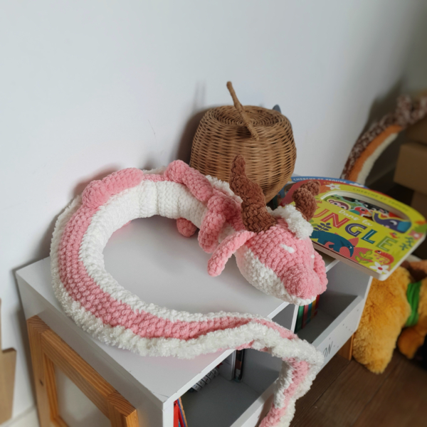 Dragon orphelin rose en laine fait main, posé en boule sur une table – création artisanale Les Doudous de Woolfy