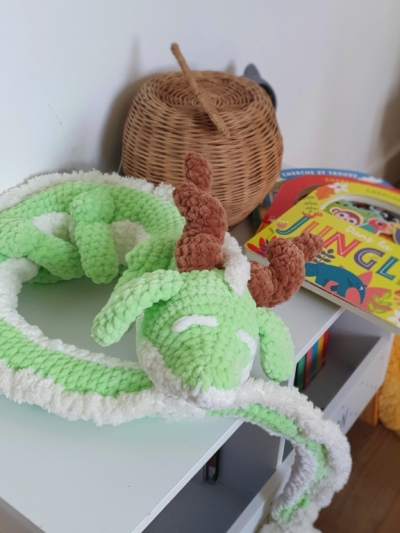 Dragon orphelin vert et blanc en laine, posé sur une table en boule