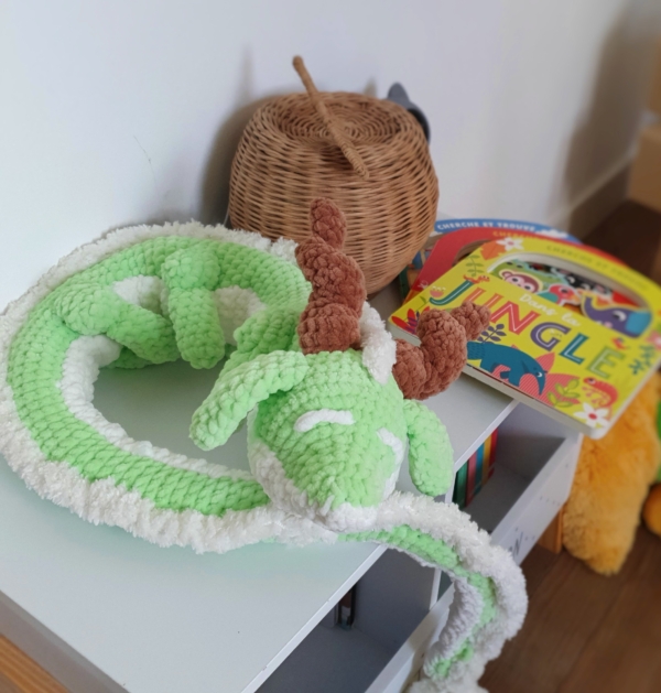 Dragon orphelin vert et blanc en laine, posé sur une table en boule
